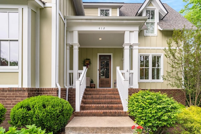 view of exterior entry featuring board and batten siding, brick siding, and a shingled roof