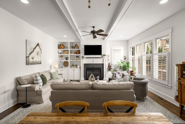 living area with a glass covered fireplace, baseboards, ceiling fan, and wood finished floors