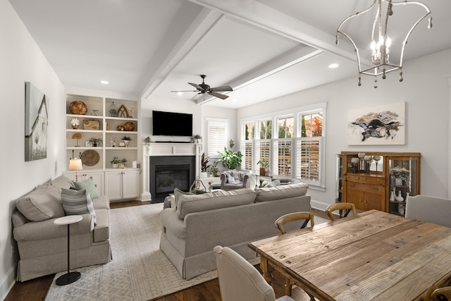 living area featuring baseboards, ceiling fan with notable chandelier, a glass covered fireplace, recessed lighting, and dark wood-type flooring