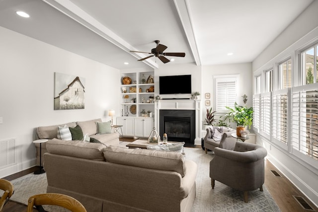living room featuring ceiling fan, visible vents, a fireplace with flush hearth, wood finished floors, and baseboards