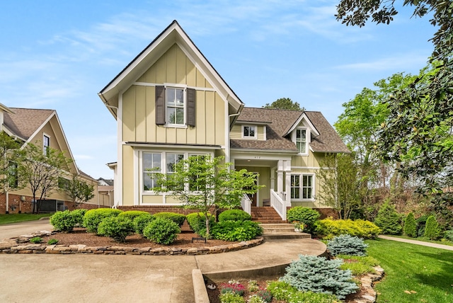craftsman-style home with board and batten siding, brick siding, a shingled roof, and a front lawn