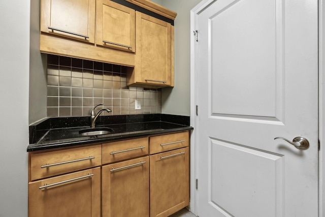 kitchen featuring a sink, backsplash, and dark stone countertops