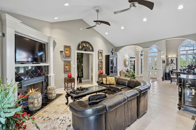 living room with light tile patterned flooring, ceiling fan, arched walkways, high vaulted ceiling, and decorative columns