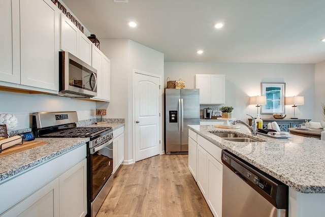 kitchen with light stone countertops, appliances with stainless steel finishes, a sink, light wood finished floors, and a center island with sink