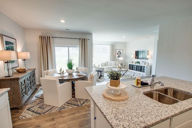 kitchen with light wood-type flooring, a sink, light stone counters, open floor plan, and white cabinetry