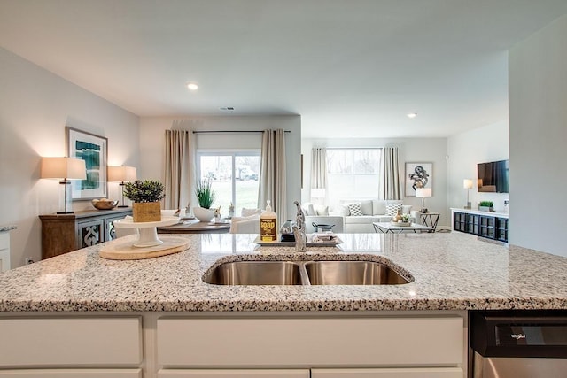 kitchen with white cabinets, light stone counters, a sink, open floor plan, and dishwashing machine