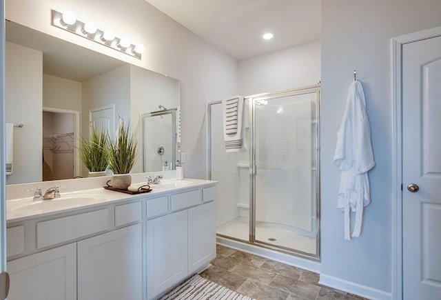 bathroom with double vanity, a sink, a walk in closet, and a stall shower