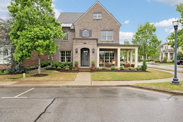traditional-style house featuring brick siding, a front yard, and a standing seam roof