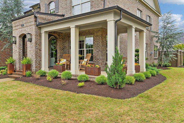 property entrance with fence, a yard, a porch, and brick siding