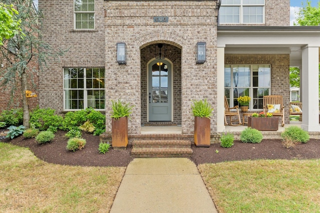 property entrance featuring brick siding, a lawn, and a porch
