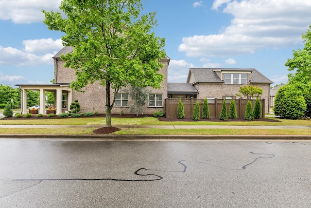 view of front of property featuring brick siding, fence, and a front lawn