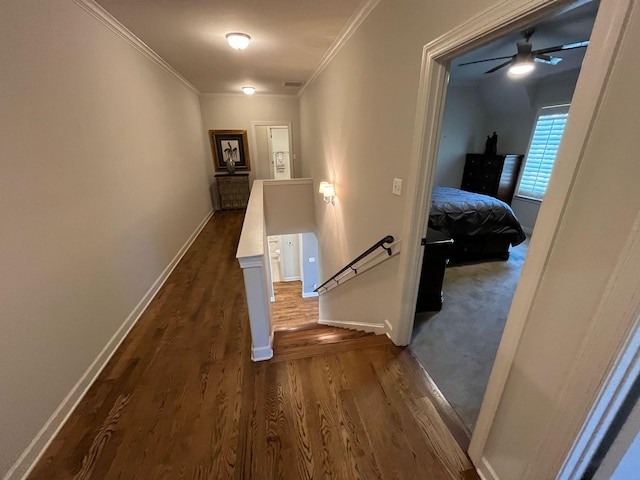 hallway featuring dark wood-style flooring, visible vents, baseboards, an upstairs landing, and ornamental molding