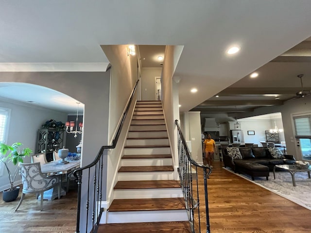 staircase featuring an inviting chandelier, wood finished floors, baseboards, recessed lighting, and arched walkways