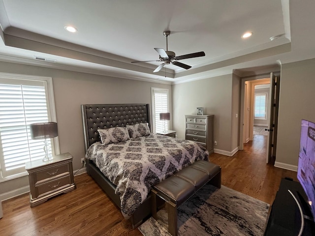 bedroom featuring a tray ceiling, visible vents, multiple windows, and wood finished floors