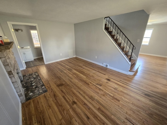 unfurnished living room featuring visible vents, baseboards, wood finished floors, and stairway