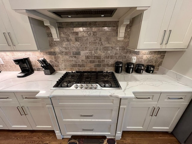 kitchen featuring stainless steel gas stovetop, decorative backsplash, ventilation hood, and light stone countertops