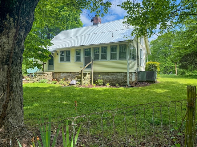 back of house with a yard, central AC, a chimney, and metal roof