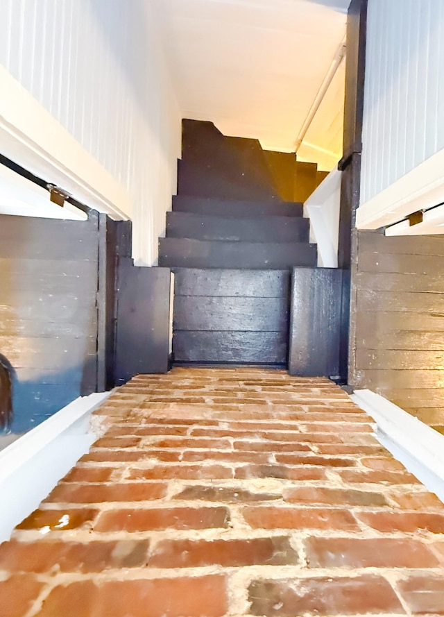 stairway featuring brick floor and wooden walls