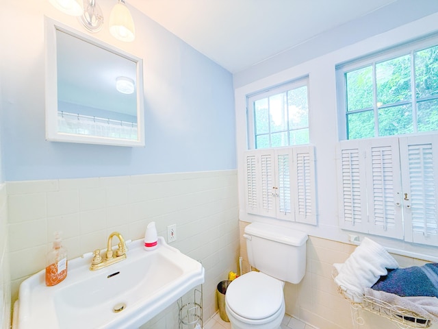 bathroom with a sink, a wainscoted wall, toilet, and tile walls