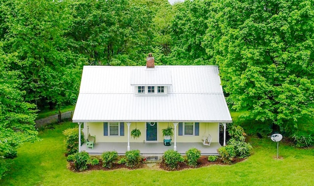 view of front facade with a porch, a front lawn, a chimney, and metal roof