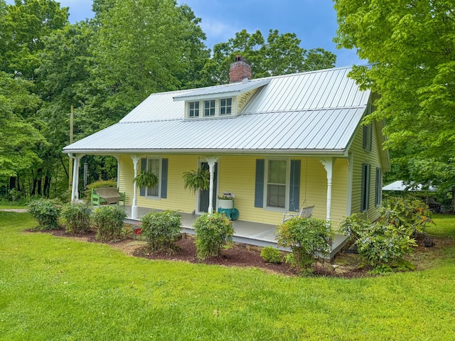 view of front facade featuring a chimney, a porch, a front lawn, and metal roof