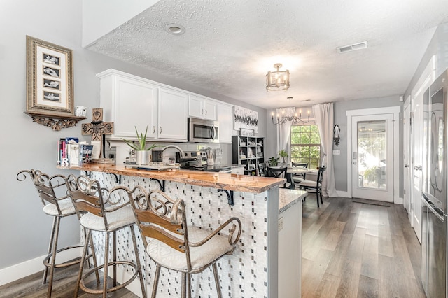 kitchen featuring appliances with stainless steel finishes, an inviting chandelier, a textured ceiling, a peninsula, and wood finished floors