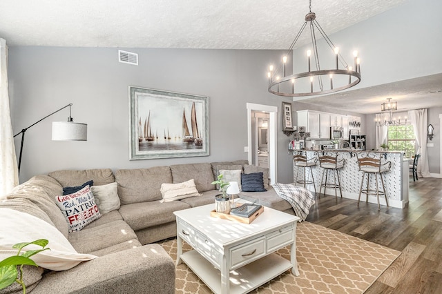 living area with a textured ceiling, a chandelier, lofted ceiling, dark wood-type flooring, and visible vents