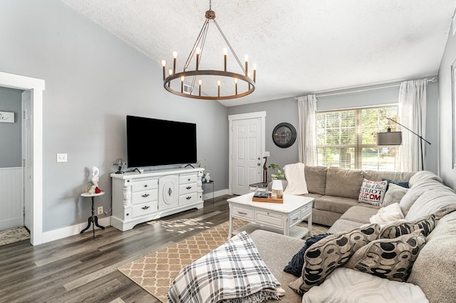 living room featuring an inviting chandelier, a textured ceiling, baseboards, wood finished floors, and vaulted ceiling
