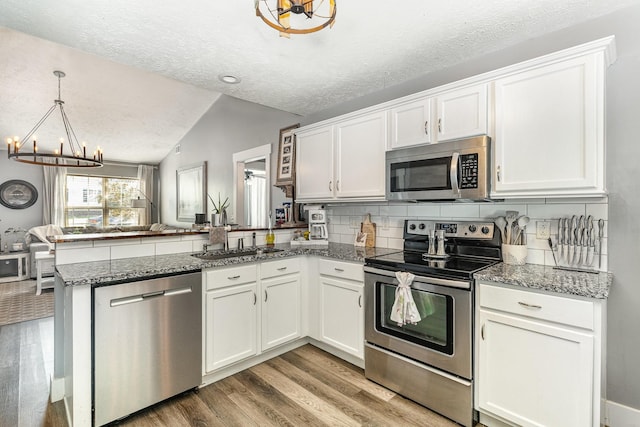 kitchen with a peninsula, a textured ceiling, a sink, appliances with stainless steel finishes, and a notable chandelier