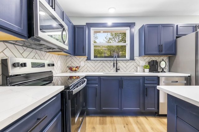 kitchen featuring decorative backsplash, blue cabinets, a sink, light wood-style flooring, and stainless steel appliances