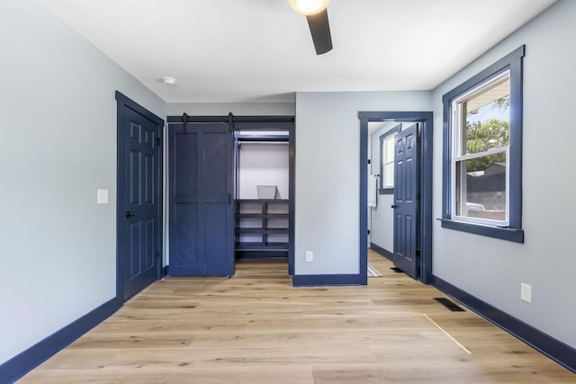 unfurnished bedroom featuring visible vents, baseboards, a barn door, a ceiling fan, and light wood finished floors