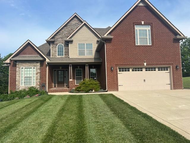 view of front of property featuring a front yard, driveway, a garage, and stone siding