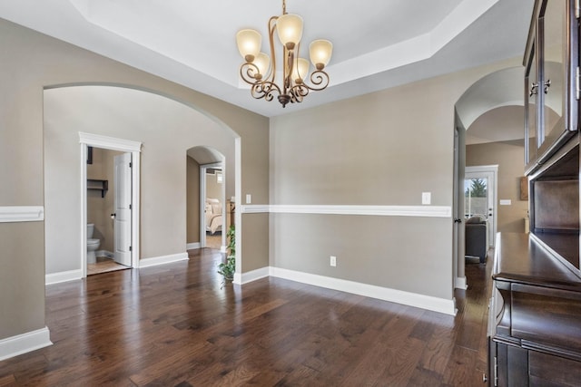 unfurnished dining area featuring arched walkways, dark wood-type flooring, baseboards, and a chandelier