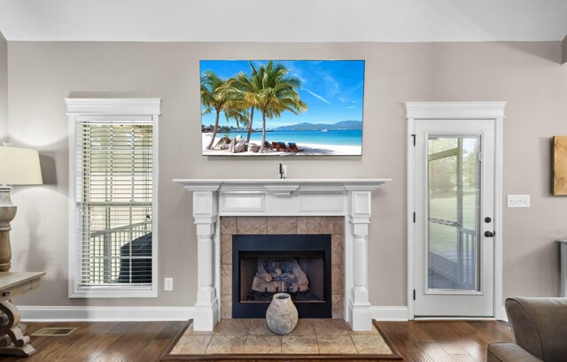 living area with wood finished floors, a tiled fireplace, and baseboards