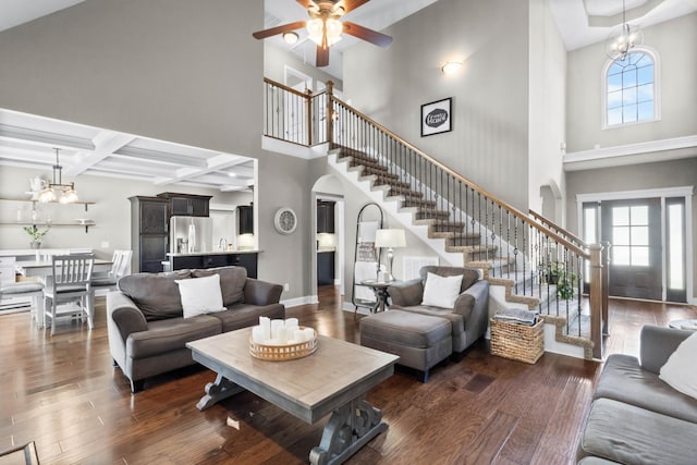 living room with stairway, a chandelier, healthy amount of natural light, dark wood-style flooring, and a high ceiling