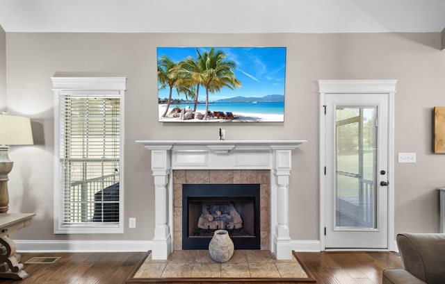 living area with wood finished floors, a tiled fireplace, and baseboards