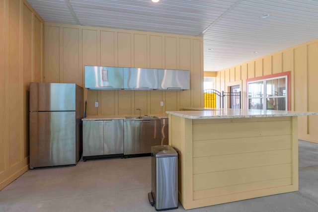 kitchen featuring freestanding refrigerator, a sink, light stone countertops, a kitchen island, and cream cabinets
