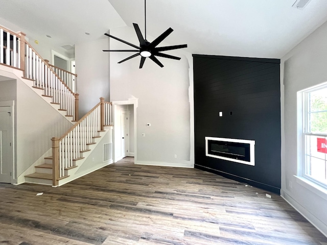 unfurnished living room with ceiling fan, wood finished floors, stairway, and high vaulted ceiling
