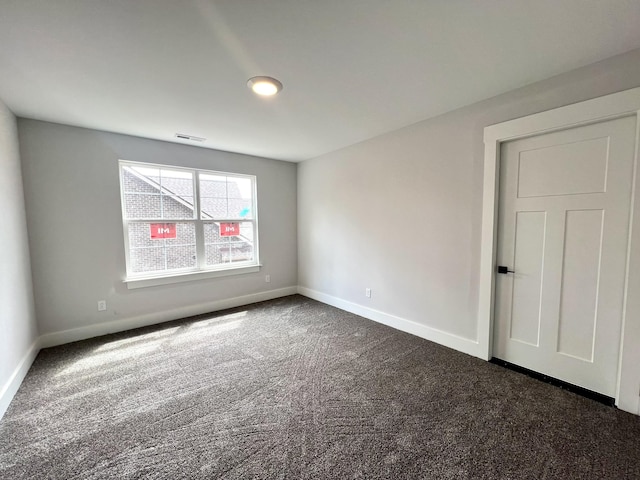 spare room featuring baseboards, dark carpet, and visible vents