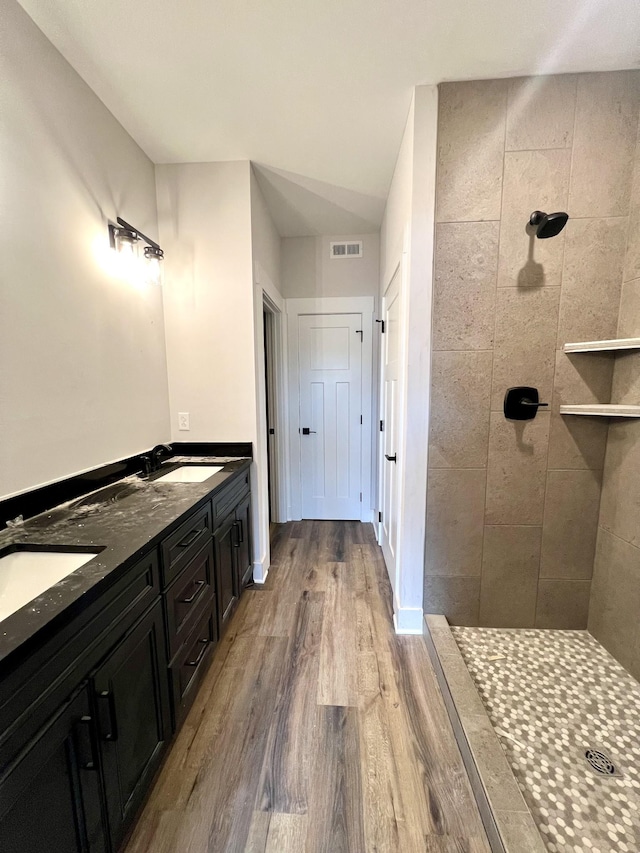 full bath featuring visible vents, a sink, wood finished floors, and a tile shower