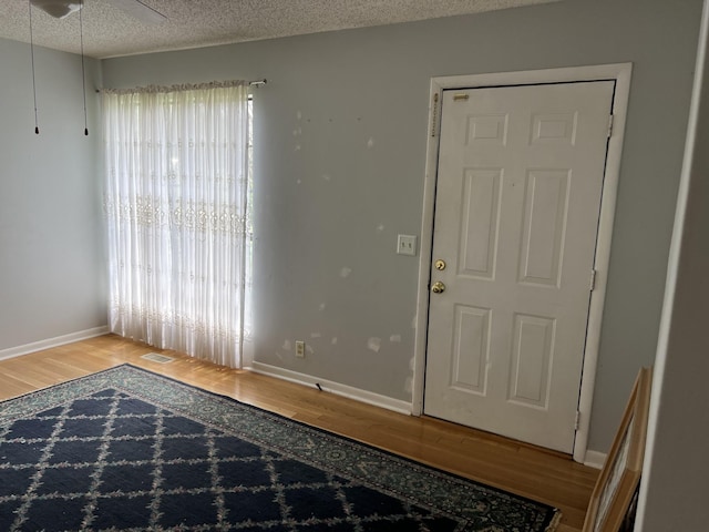 foyer with baseboards, a textured ceiling, wood finished floors, and visible vents