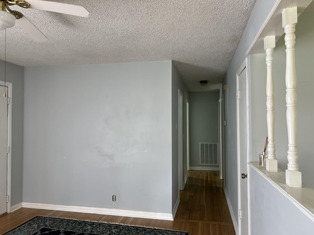 corridor featuring wood finished floors, baseboards, a textured ceiling, and visible vents