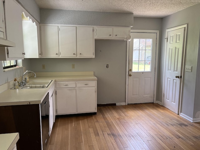 kitchen with light wood-type flooring, dishwasher, light countertops, a sink, and white cabinets