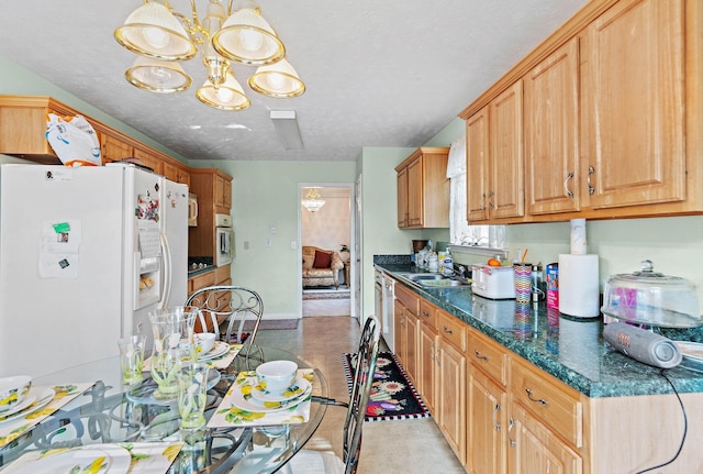 kitchen featuring an inviting chandelier, a sink, white appliances, a textured ceiling, and baseboards