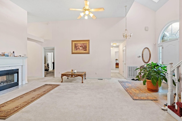 carpeted foyer with a premium fireplace, high vaulted ceiling, ceiling fan with notable chandelier, visible vents, and stairway