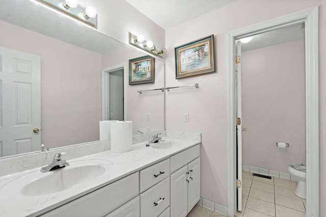 bathroom with toilet, double vanity, tile patterned floors, and a sink