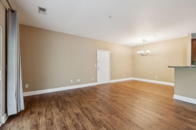 unfurnished room featuring baseboards, a chandelier, wood finished floors, and visible vents