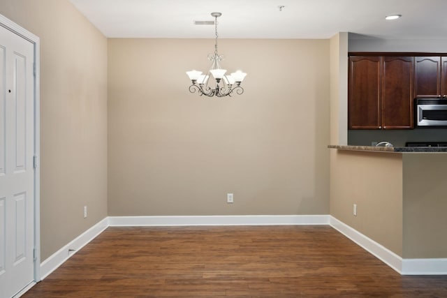 unfurnished dining area with dark wood-style flooring, baseboards, a notable chandelier, and visible vents
