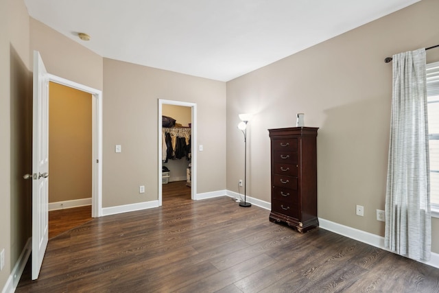 unfurnished bedroom with baseboards, a closet, dark wood-style floors, and a spacious closet