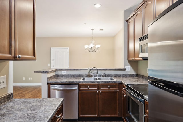 kitchen featuring a peninsula, dark wood-type flooring, a chandelier, a sink, and stainless steel appliances